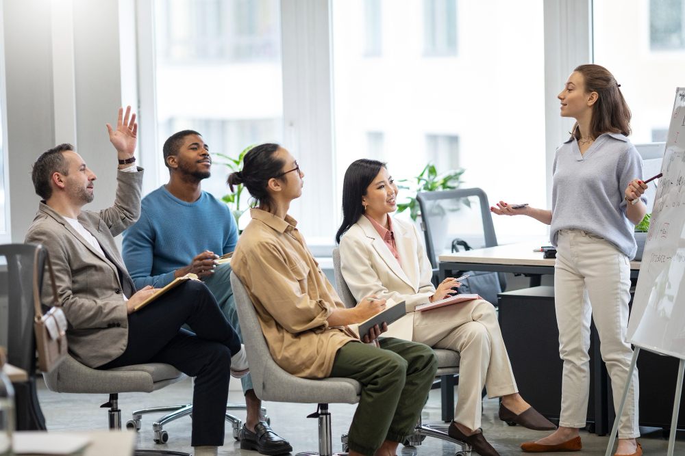 Comunicação e Liderança Reunião de equipe em ambiente corporativo com uma mulher apresentando ideias para colegas sentados, promovendo colaboração e discussão estratégica.