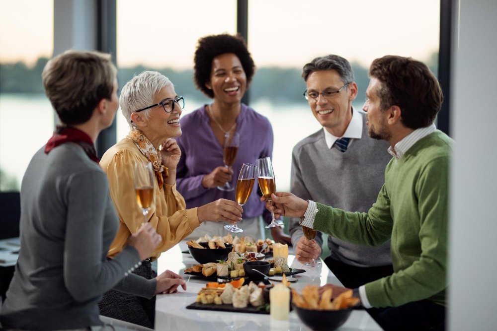 Grupo de profissionais de diferentes idades brindando com taças de vinho durante um encontro social em ambiente corporativo