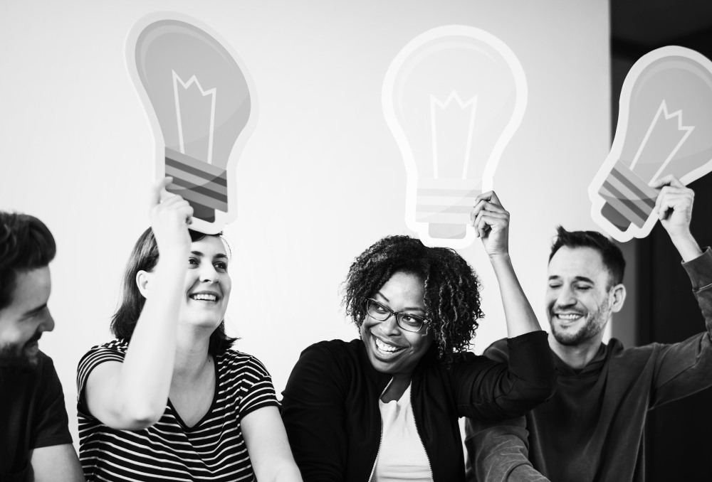Grupo de pessoas felizes segurando lâmpadas de desenho, simbolizando ideias criativas e inovação em um ambiente colaborativo.