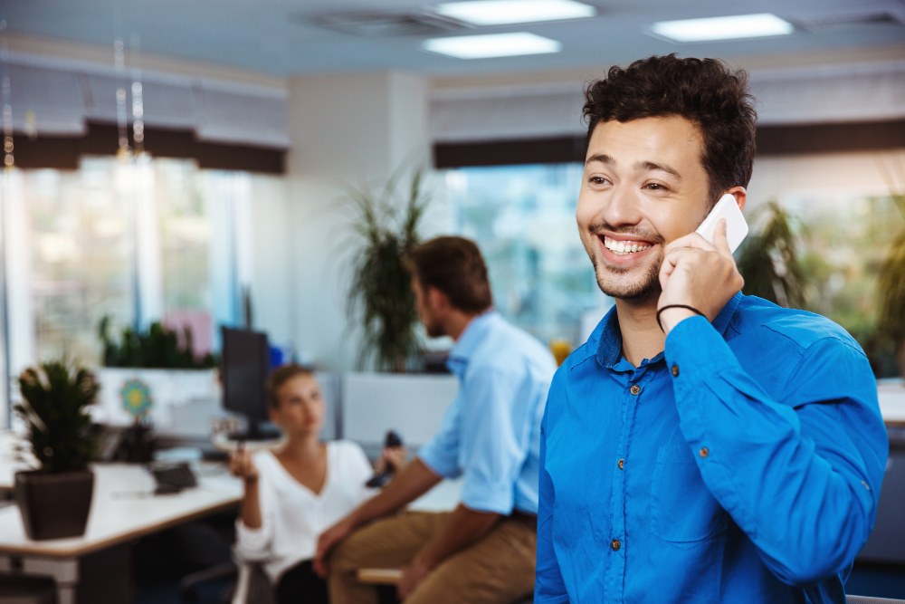 Profissional sorrindo ao telefone em um escritório, representando um ambiente positivo gerado pelo desenvolvimento de lideranças.