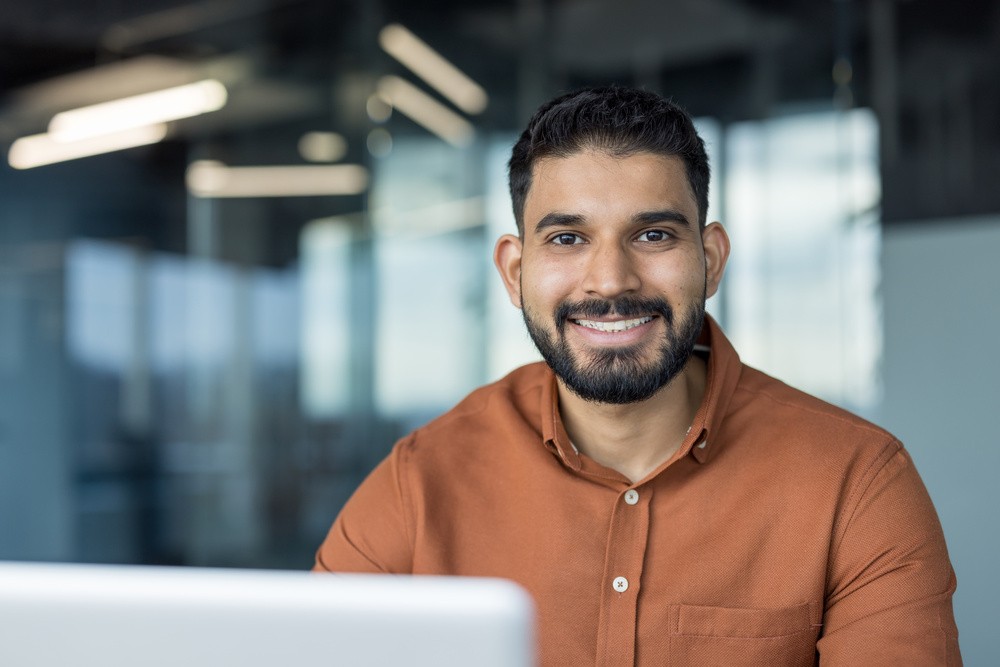 Profissional sorrindo em ambiente corporativo moderno, representando a alta direção em reunião estratégica diante do computador.